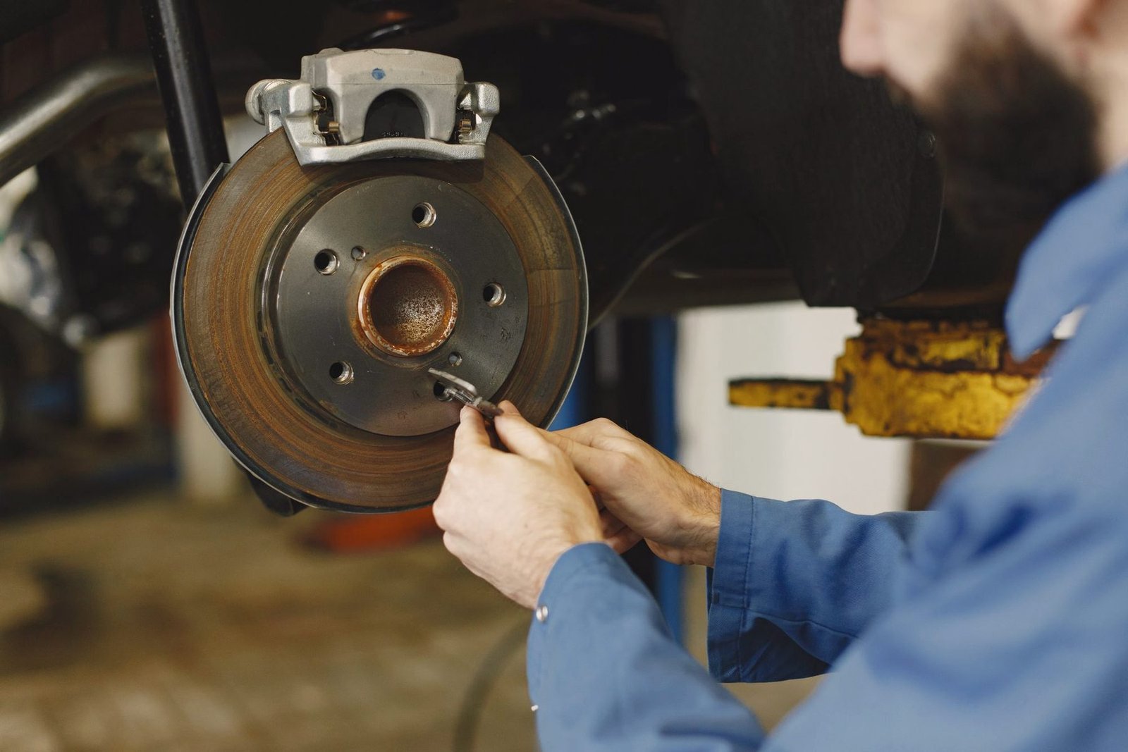 Gloved hands working on a brake rotor and hub at the wheel arch.