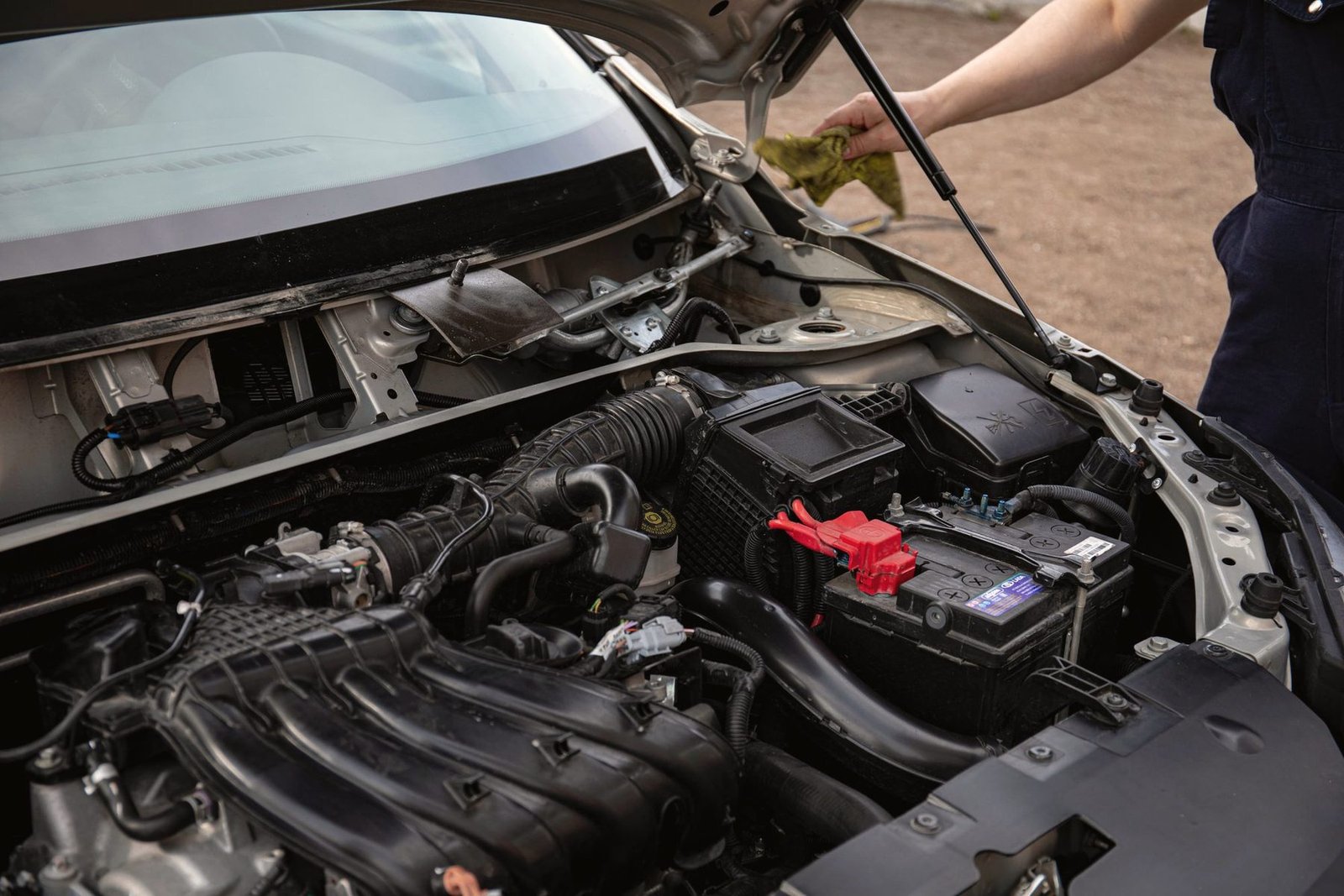 Hands checking the battery and wiring in an open engine bay.