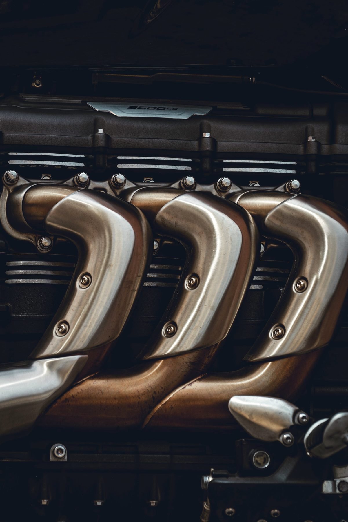 Polished exhaust header pipes curving away from an engine block.