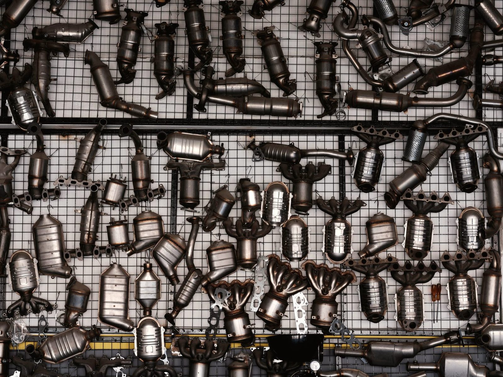 A workshop wall hung with rows of mufflers, resonators and exhaust clamps.