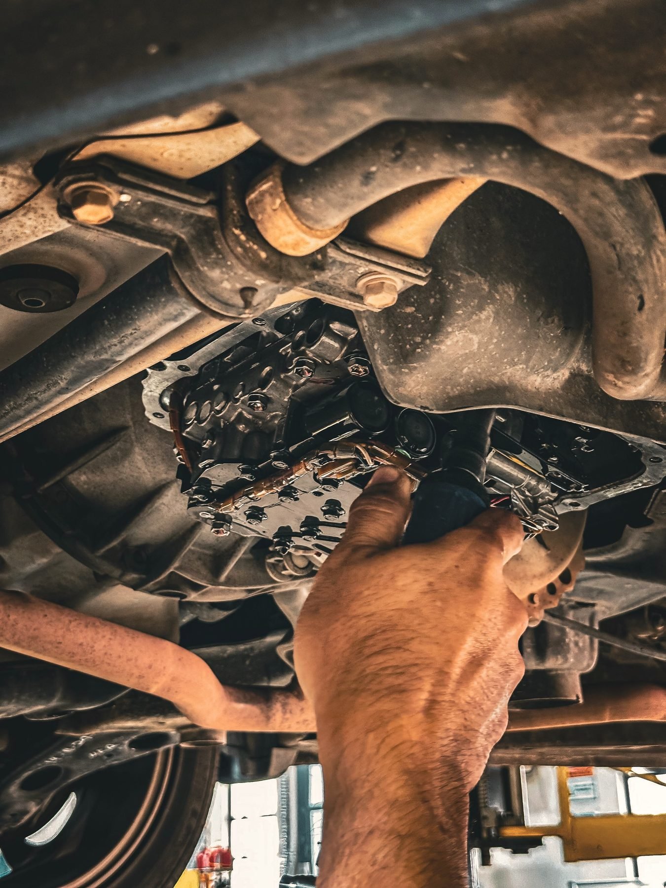 Hands reaching up into a vehicle chassis with a wrench, working on rusted components.