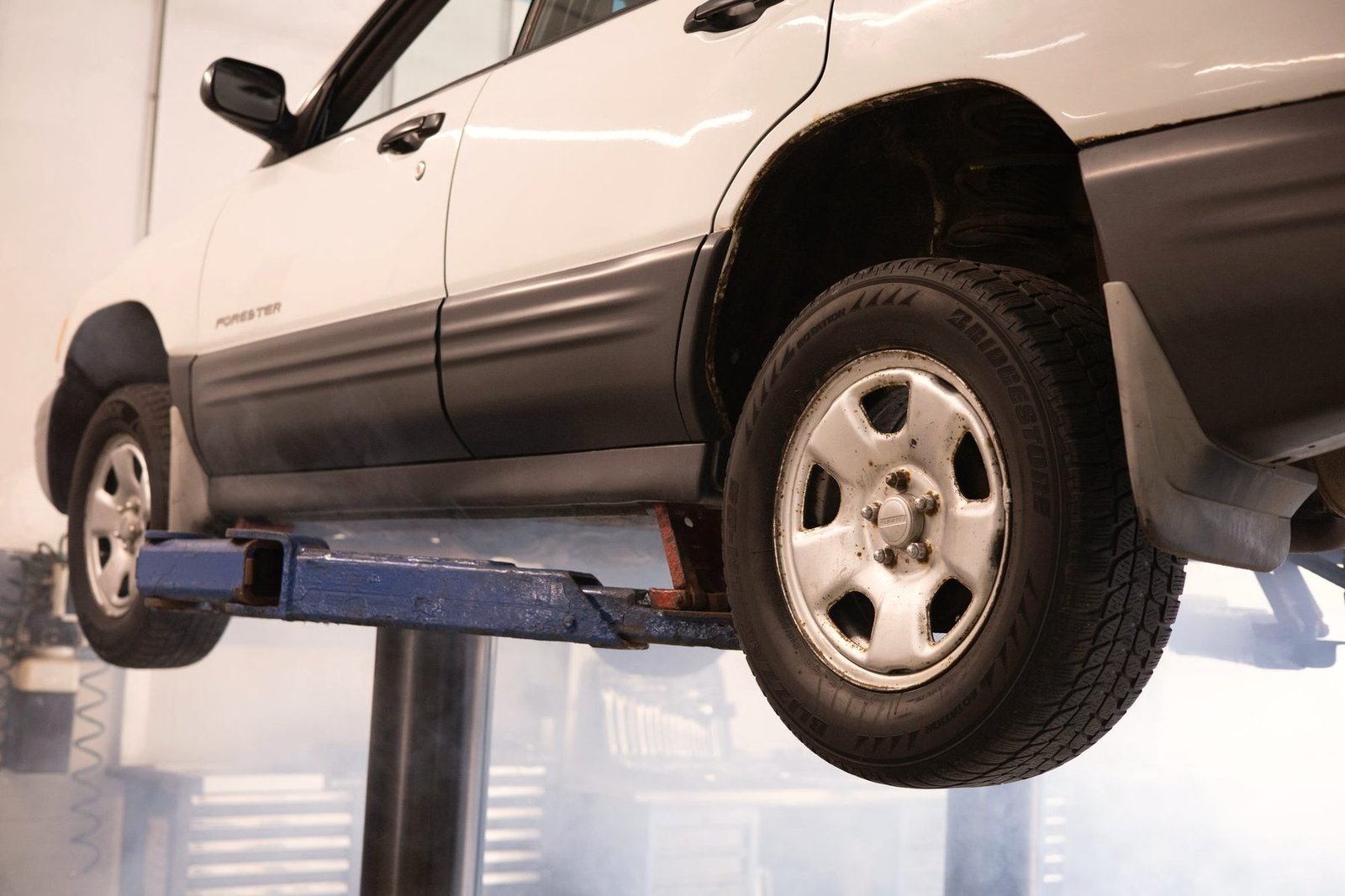 A pickup truck raised on a two post lift inside a workshop.