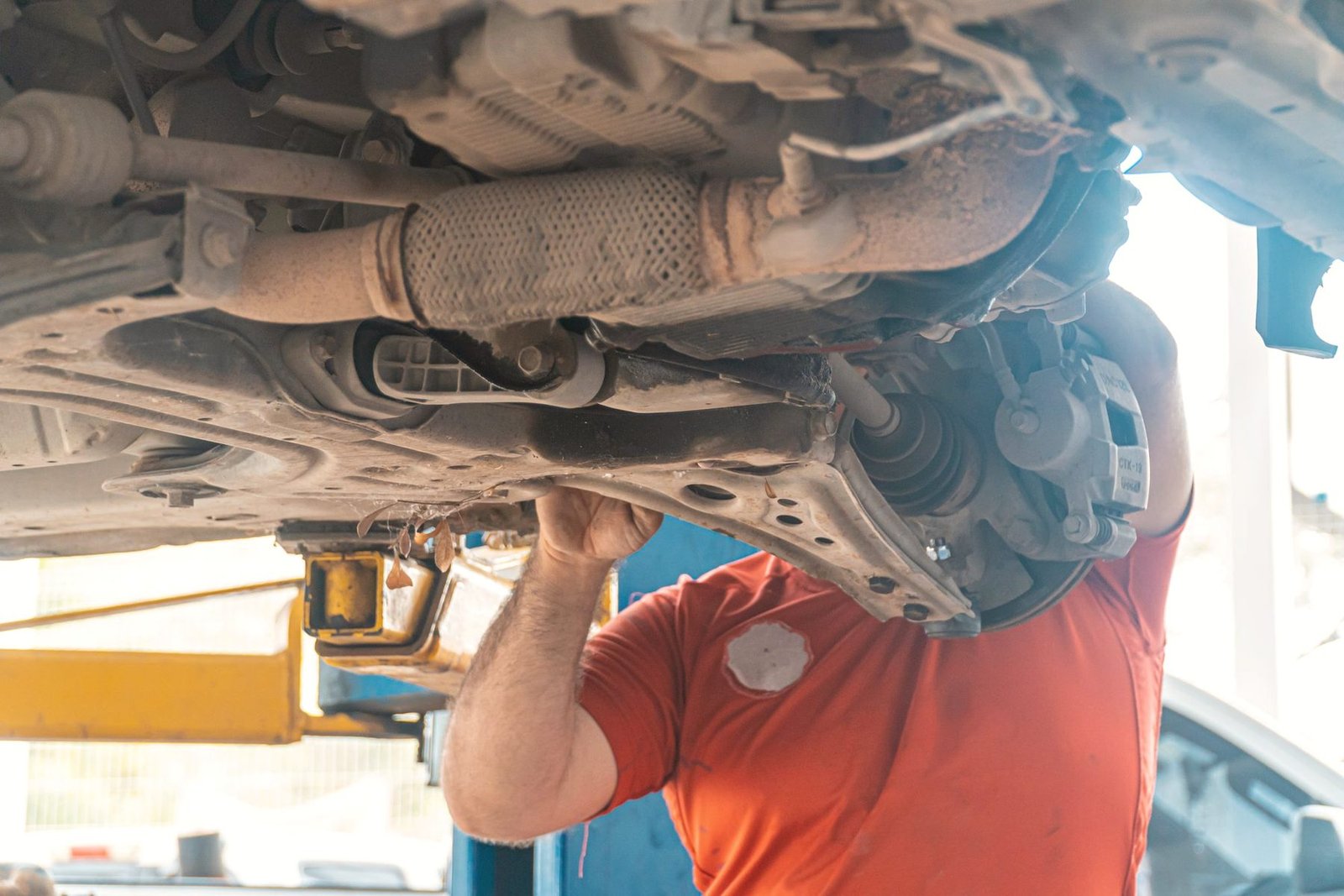 A technician in orange working on the exhaust of a car raised on a two post lift.